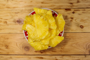 Pieces of pineapple in a plate on wooden table. Top view