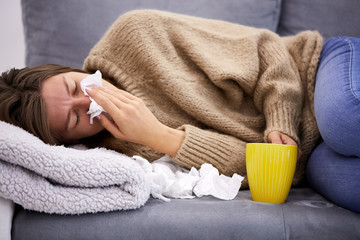 Sick girl holding tissue and holding stomach and tea.