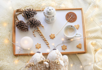 Cozy monochrome pastel colors flat lay. Top view of soft deer slippers, cappuccino, candle, lollipop with gingerbread man, Christmas candy cane, star cookies, pine cones with garland on fur rug