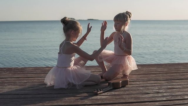 Happy girls in beautiful dresses are playing on the sea pier. In the background sea sunset. Wooden pier