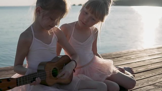 Beautiful girls play the guitar and sing funny songs. Children play on the sea coast. Evening time, calm sea.