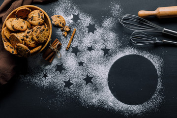 view from above of cookies in bowl, whisks and rolling pin on table covered by flour with symbol of...