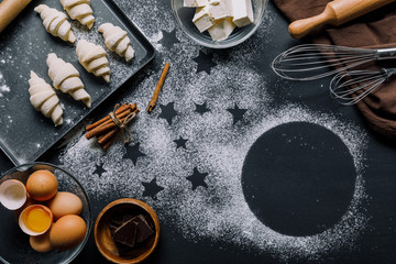 view from above of tray with dough for croissants and ingredients on table covered by flour with...