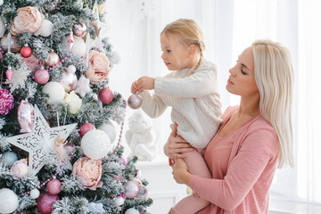 Merry Christmas and Happy Holidays. Mom and daughter decorate the Christmas pink tree indoors. new...