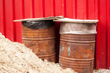 Naklejka premium two metal rusty barrels covered with boards against red metal wall
