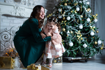 Obraz premium Merry Christmas and happy holidays. Mother and daughter having fun near the Christmas tree with gifts