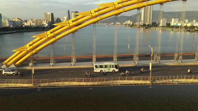 A tracking aerial shot of a bus and motorbikes crossing over the famous dragon bridge in Danang Vietnam.
