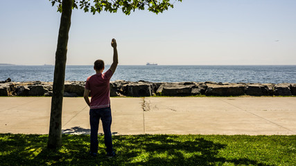 A sad man or boy standing alone on the seaside and waving her hand to the distant ship with feeling...