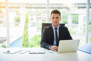 Portrait of young businessman working with laptop and communication device, tablet and mobile or smartphone on desk in office.