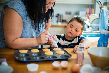 Mother helping son to put frosting onto cupcakes