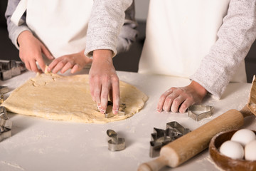 partial view of children in aprons cutting out dough for cookies at table in kitchen