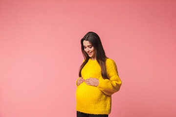 Beautiful young pregnant emotional woman posing isolated over pink background.