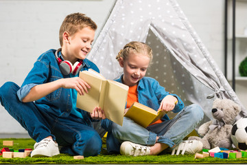 smiling boy with headphones over neck showing book to little sister near wigwam at home © LIGHTFIELD STUDIOS