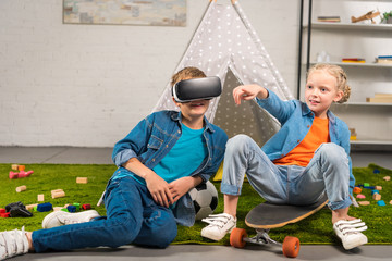 boy using virtual reality headset  and his sister pointing by finger while sitting on skateboard near wigwam at home © LIGHTFIELD STUDIOS