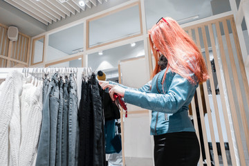 red hair young girl in a blue leather jacket chooses pants for sale.