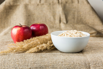 Oatmeal in white plate with red apples and spike on textile background. Healthy eating