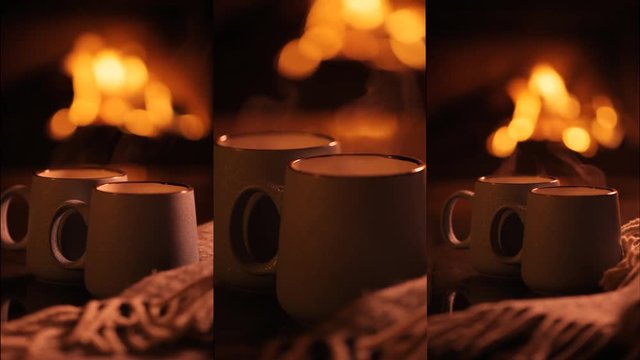 Vertical videos. Steam from a cups with a hot cocoa on the fireplace background.  Slow motion.