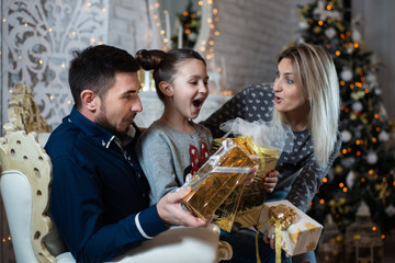 Christmas photo of happy family with gift boxes on background of decorated Christmas tree. Family celebrates New year
