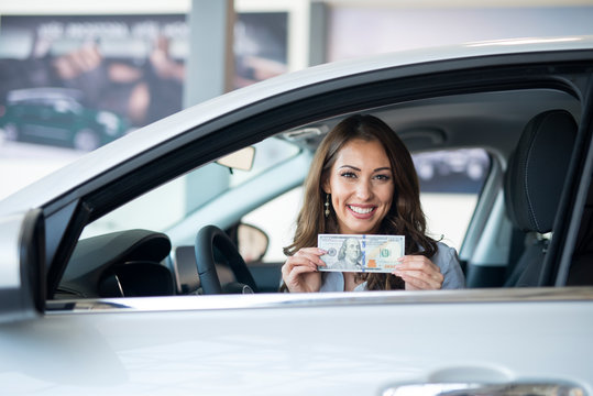 Cheerful woman sitting in the new car holding US dollar banknote. Car insurance and rental concept.