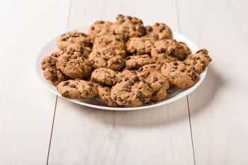 Dish of gluten-free craft biscuits with chocolate nuggets over white wooden background