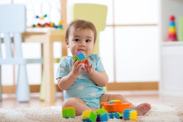 Baby boy playing with colorful plastic bricks on the carpet on floor. Toddler having fun and building out of constructor bricks. Early learning and developing toys concepts