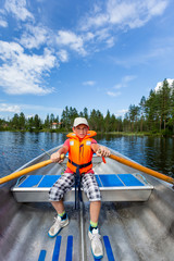 Young teenage boy rowing a rowboat on a lake with blue summer sky in the background.