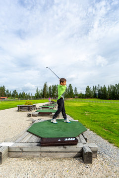 Young teenage boy outdoors at a driving range playing golf and practice his swing.
