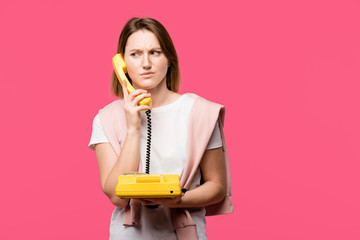 young woman with frowning eyebrows talking by handset isolated on pink