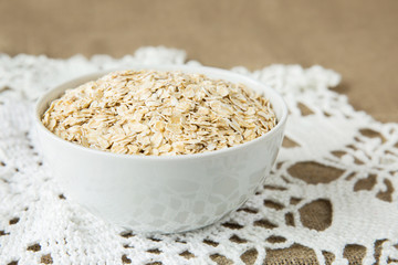 Oatmeal in white bowl on light brown textile background. Healthy eating
