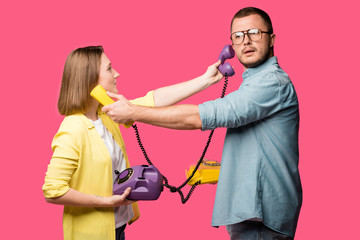 side view of young couple holding rotary phones and handsets for each other isolated on pink