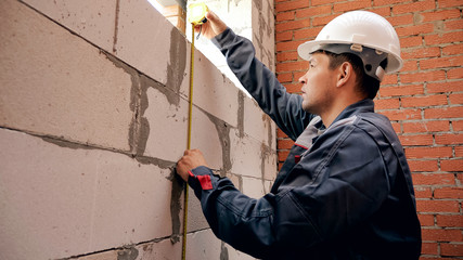 Back view of man working on site and measuring window in brick wall with ruler