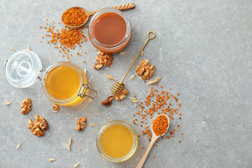 Jars with sweet honey and walnuts on grey table
