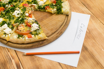 Count the calories. Sheet with the inscription Calories and lying near a pizza on a wooden background.