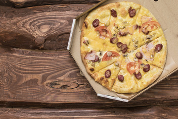 Pizza in a cardboard box on a dark wooden background.