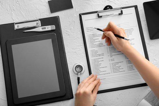 Female doctor filling in laboratory test request form on table. Health care concept