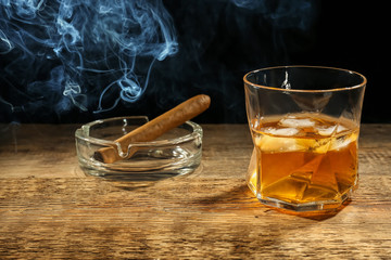 Glass of whiskey with cigar on wooden table against dark background