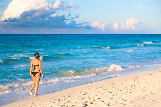 Summer vacation, tourism and relax concept. Young woman in bikini walking on exotic beach. Idyllic background.