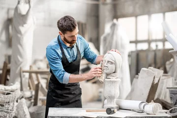 Foto op Canvas Handsome sculptor brushing stone head sculpture on the table in the atmospheric studio © rh2010