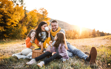 A young family with two small children having picnic in autumn nature at sunset.