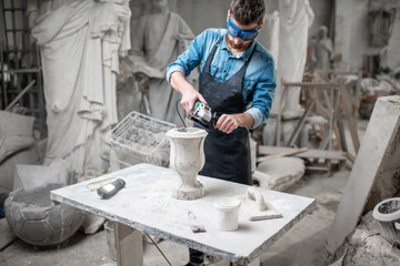 Sculptor in workware grinding stone vase at the working space in the old atmospheric studio