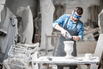 Sculptor in workware grinding stone vase at the working space in the old atmospheric studio