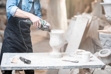 Sculptor in workware grinding stone vase at the working space in the old atmospheric studio. Cropped imaage with no face