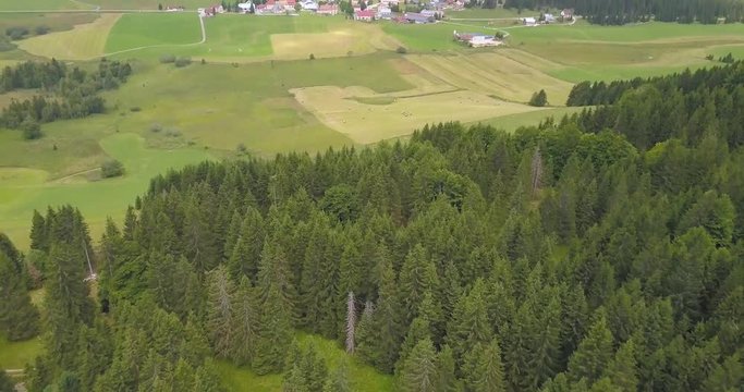 Aerial, tilt up, drone shot, over green, pine forest, revealing a small town, in the french countryside, shadows reflecting on the ground, in Chapelle des bois, Doubs and Jura regional park, in France