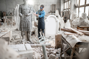 Sculptor working with big stone figure grinding with electirc grinder in the old atmospheric studio...