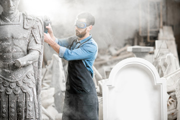 Sculptor in protective workware grinding stone sculpture with electirc grinder in the old studio with dust