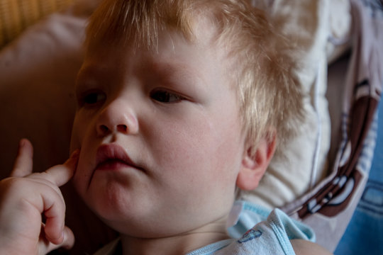 Caucasian blond boy has just woken up and is busy with himself. Child put his finger in nose. Fun kid cute face