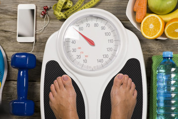 Sportive weighting on bathroom scale with sport object and healthy food around