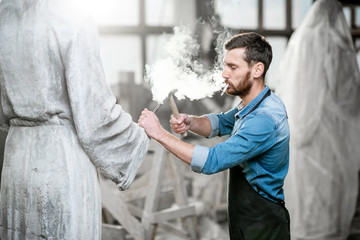 Handsome smoking sculptor beating stone sculpture with hammer and chisel in the studio