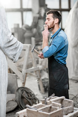 Handsome smoking sculptor beating stone sculpture with hammer and chisel in the studio