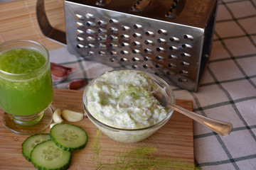 Freshly prepared tzatziki sauce on a bowl on a wooden background with cucumber drink.
